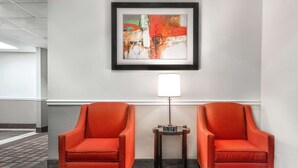 A hotel lobby with two red armchairs, a framed abstract painting, and a small table with a lamp. - Days Inn & Suites by Wyndham Dallas (Dallas)
