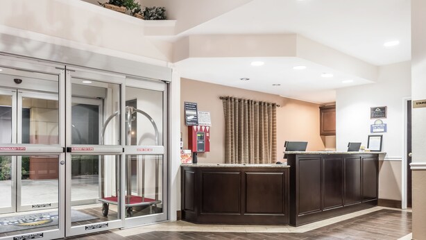 A reception area with a glass door entrance, a reception desk, a fire extinguisher, and a sign indicating the manager's office. - Days Inn & Suites by Wyndham Dallas (Dallas)