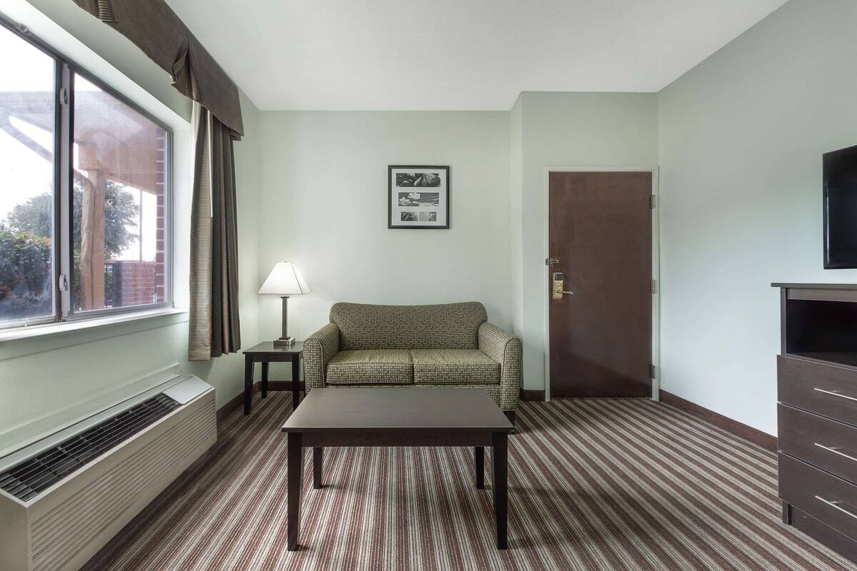 Een hotelkamer met raam, bank, tafel, lamp, deur en televisie.