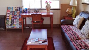 Una sala de estar con una mesa de centro de madera, un sofá con cojines estampados, un escritorio con una silla y una ventana con persianas.