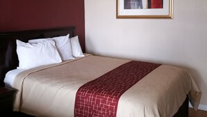 Una habitación de hotel con una cama grande, una mesita de noche, un cuadro enmarcado en la pared y una pared de acento roja.