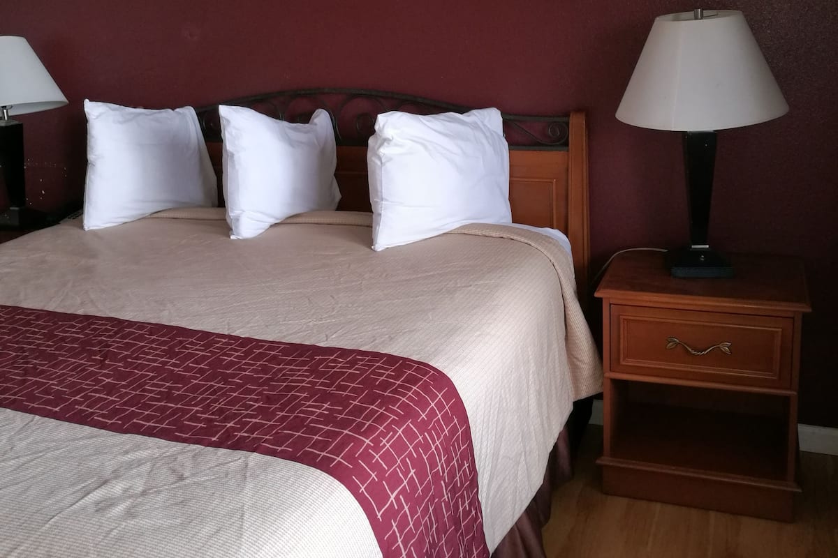 Una habitación de hotel con una cama, dos mesitas de noche, una lámpara y una pared roja.