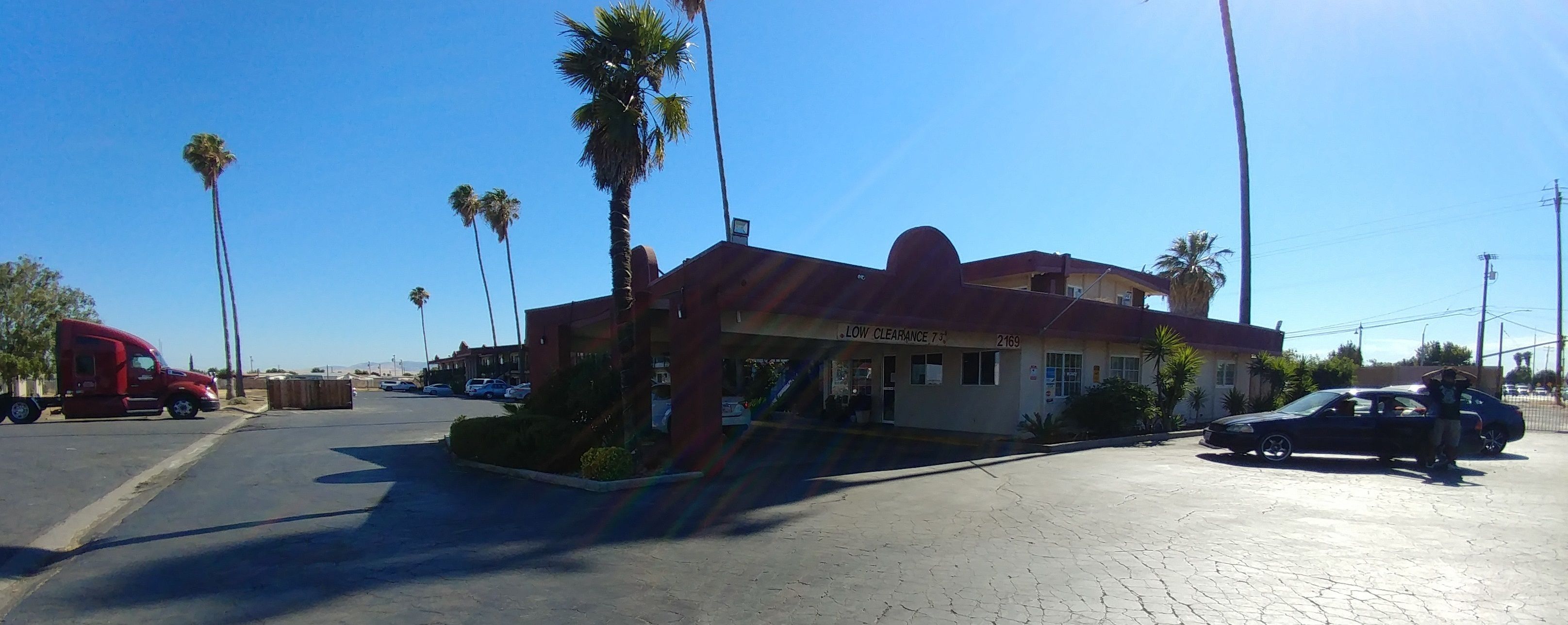 A building with a low clearance sign, palm trees, and parked vehicles.
