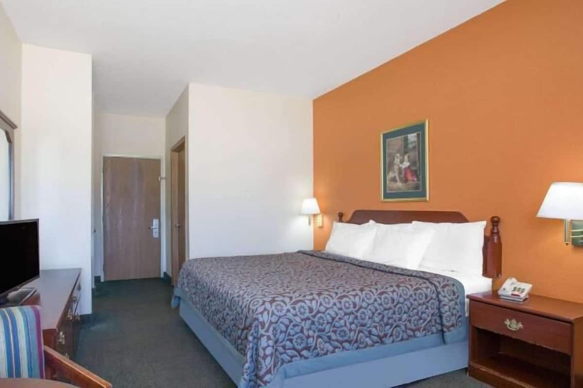 A hotel room with a bed, bedside lamps, a television, a desk, and a chair.