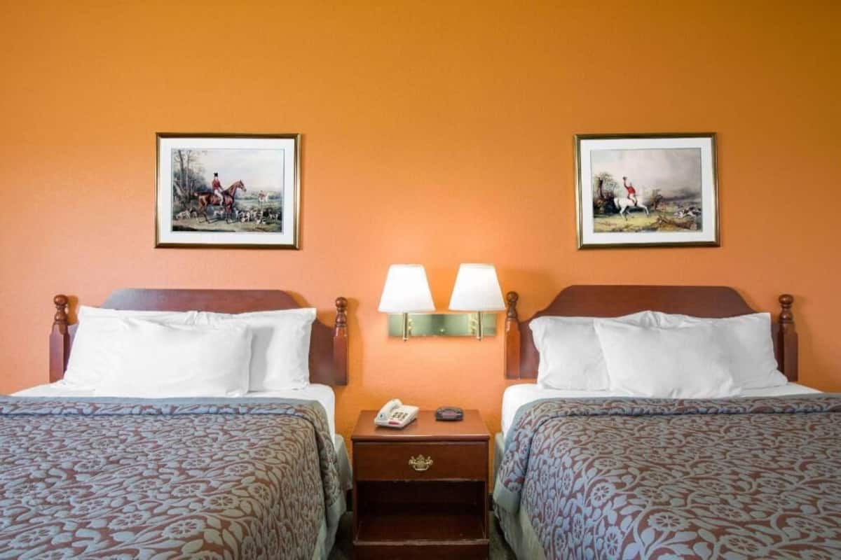 A hotel room with two beds, a nightstand with lamps, and two framed pictures on the wall.
