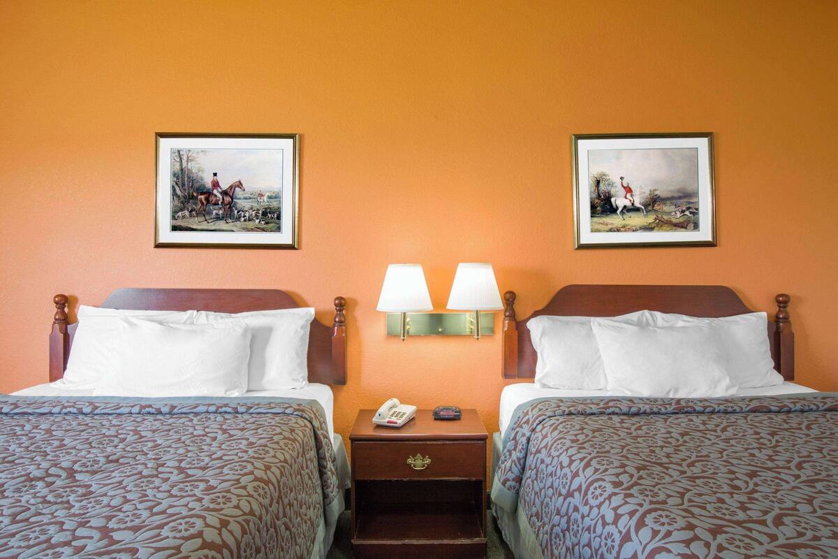 A hotel room with two beds, a nightstand with a lamp, and two framed pictures on the wall.