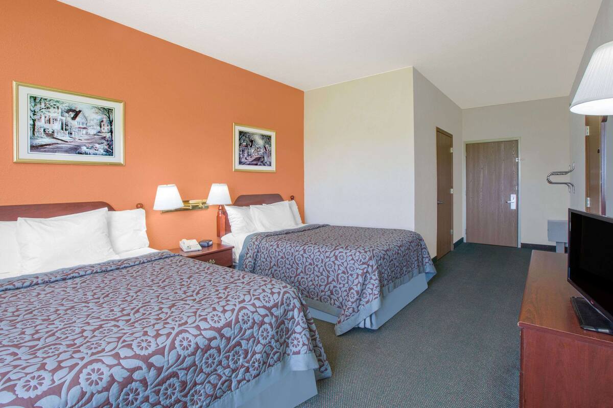 A hotel room with two beds, a television, a desk, and two framed pictures on the wall.