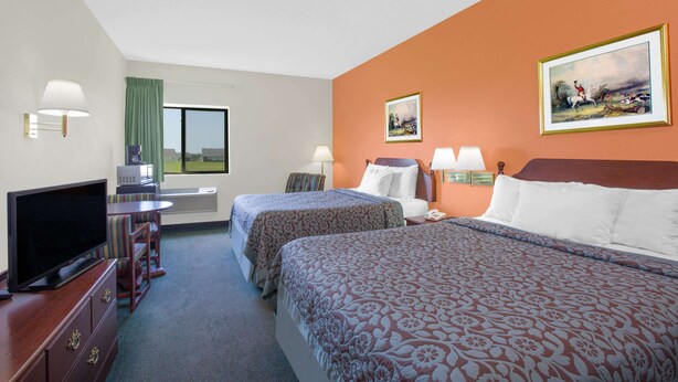 A hotel room with two beds, a television, a desk with a chair, and a window with curtains.