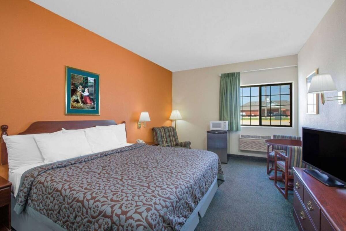 A hotel room with a large bed, a television, a desk with a lamp, and a window with a view.