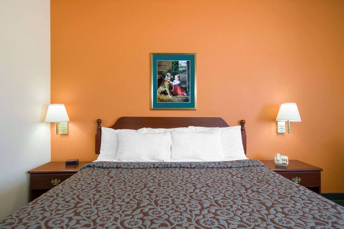 A hotel room with a large bed, two bedside tables, a nightstand, a wall-mounted painting, and two wall lamps.