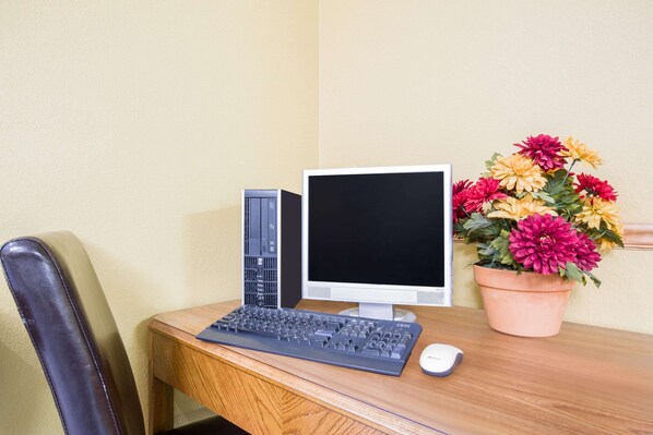 A desk with a computer setup, including a keyboard, monitor, and tower. There is a chair and a potted plant with flowers.