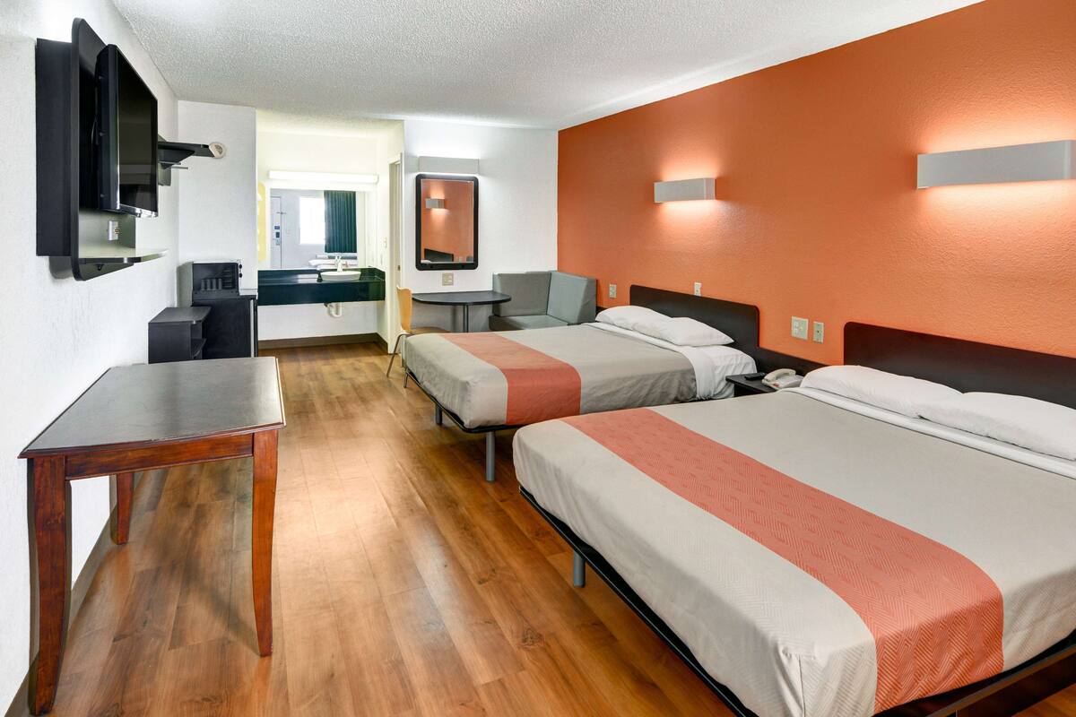 A hotel room with two beds, a desk, a chair, a TV, and a bathroom visible in the background.