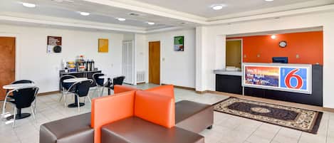 A hotel lobby with a reception desk, seating area, and a kitchenette.