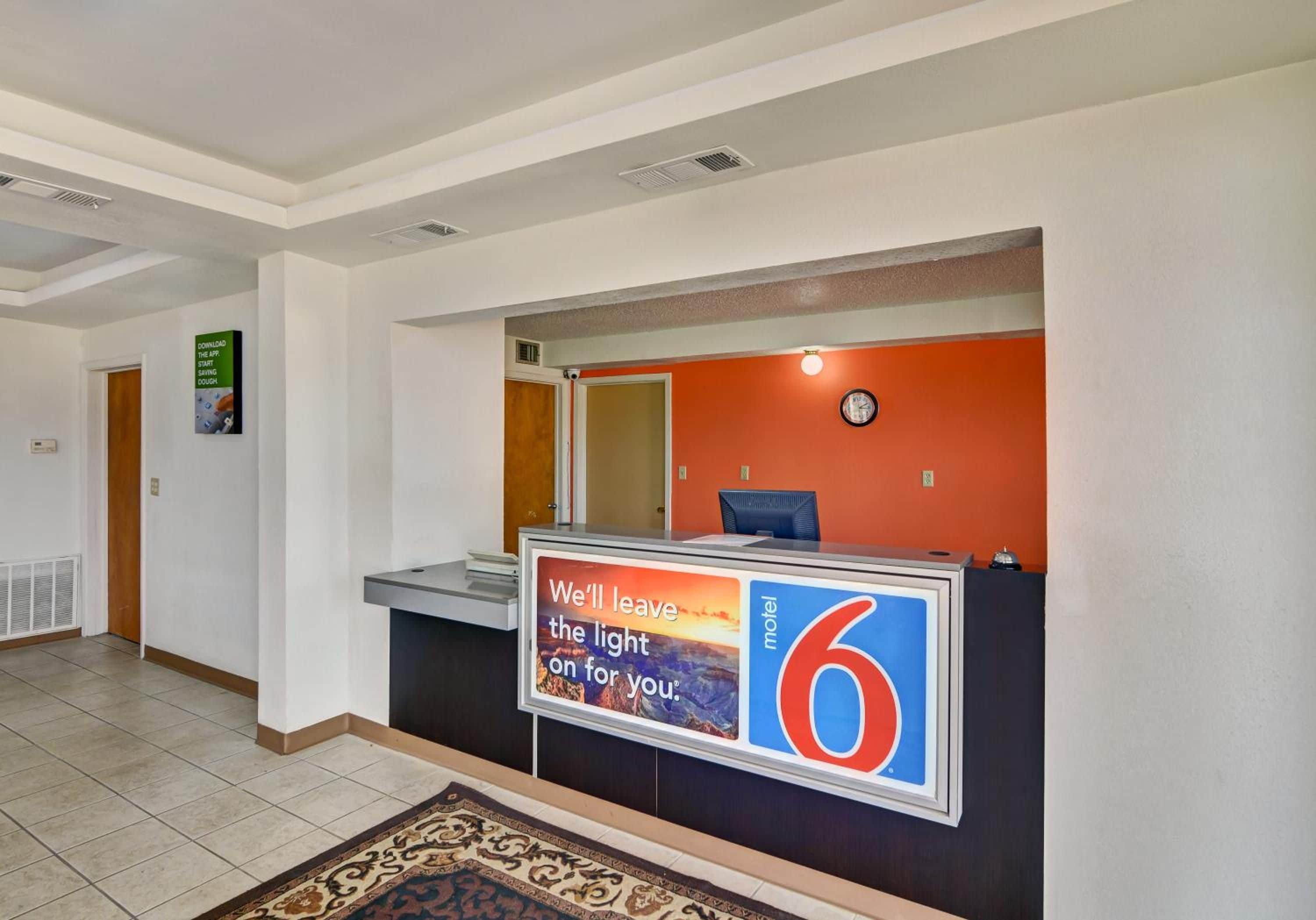 A hotel reception area with a reception desk, a clock, and a sign advertising the motel.