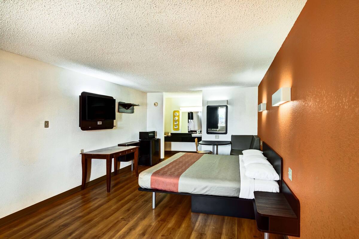 A hotel room with a bed, a desk, a chair, a TV, and a mirror.