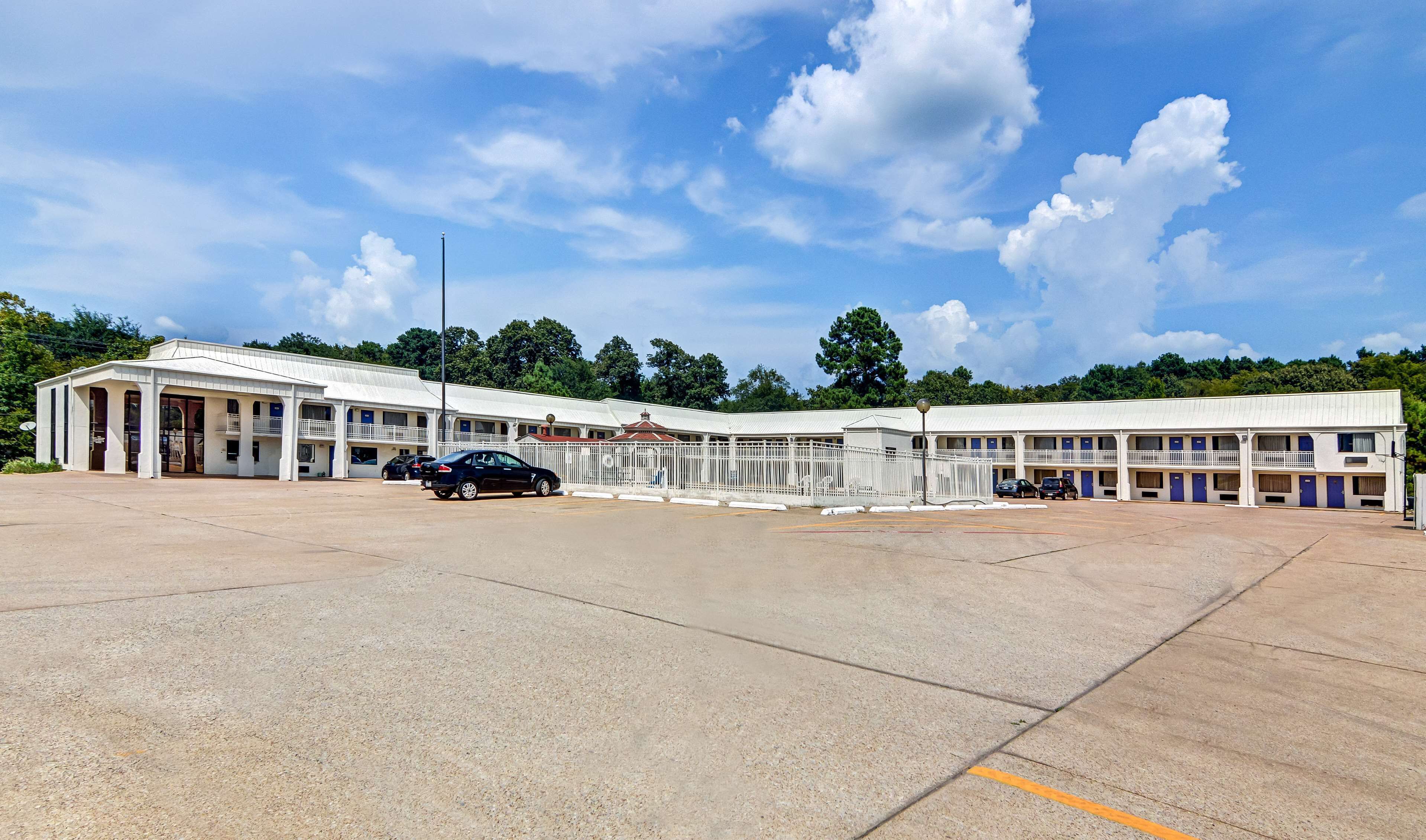 A motel with a large parking lot, multiple rooms with balconies, and a central building with a red roof.