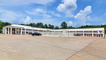 A motel with a large parking lot, multiple rooms with balconies, and a central building with a red roof.