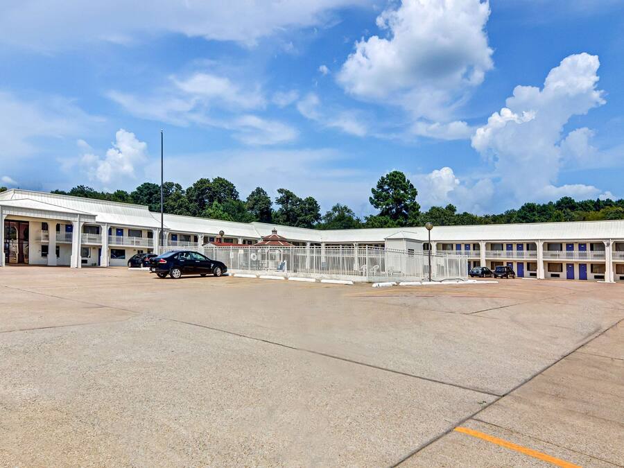 A motel with a large parking lot, multiple rooms with balconies, and a central building with a red roof.