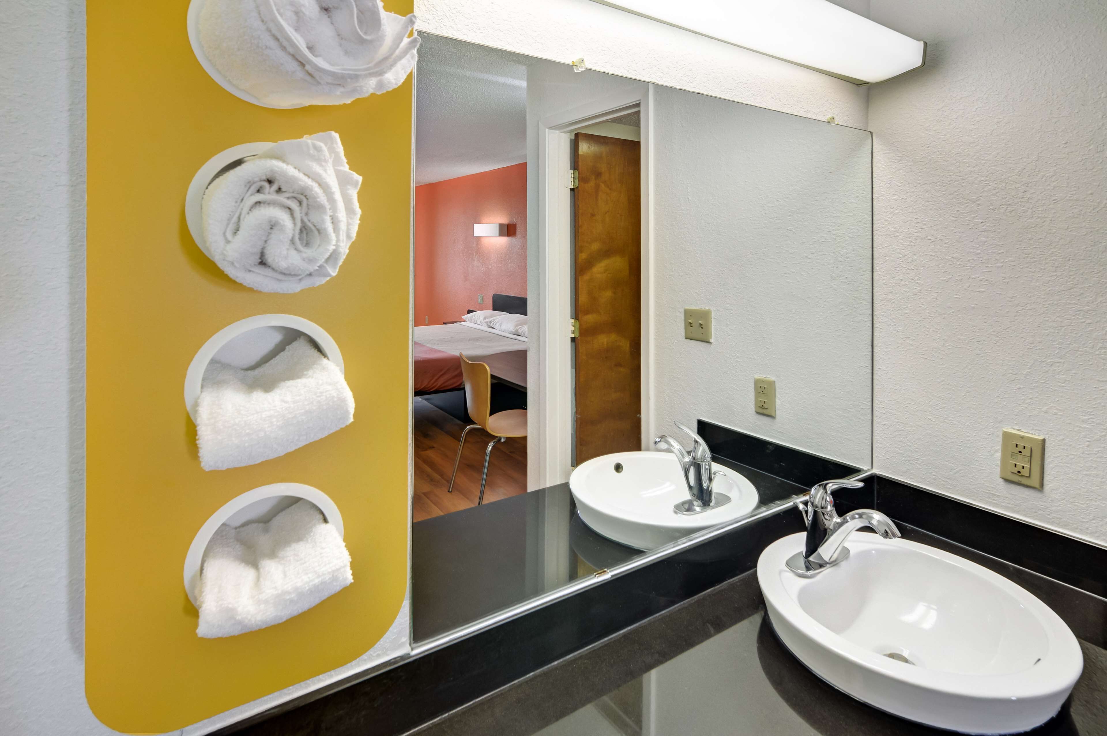 Un bagno con due lavandini, uno specchio e ganci per asciugamani su una parete gialla.