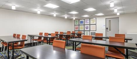 Una sala conferenze con diversi tavoli e sedie arancioni, dotata di luci a soffitto e un tappeto fantasia.