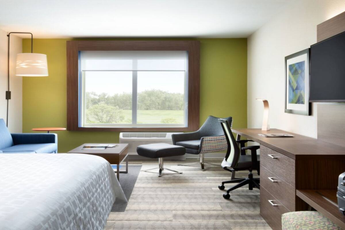 A hotel room with a bed, desk, chair, and a large window.