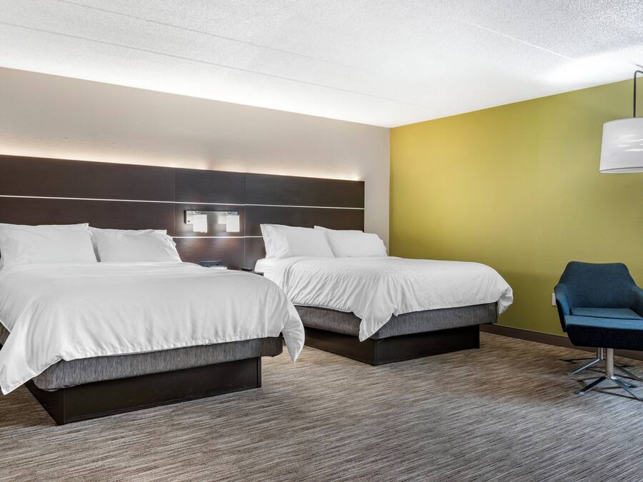 A hotel room with two beds, a nightstand, a lamp, and a chair.