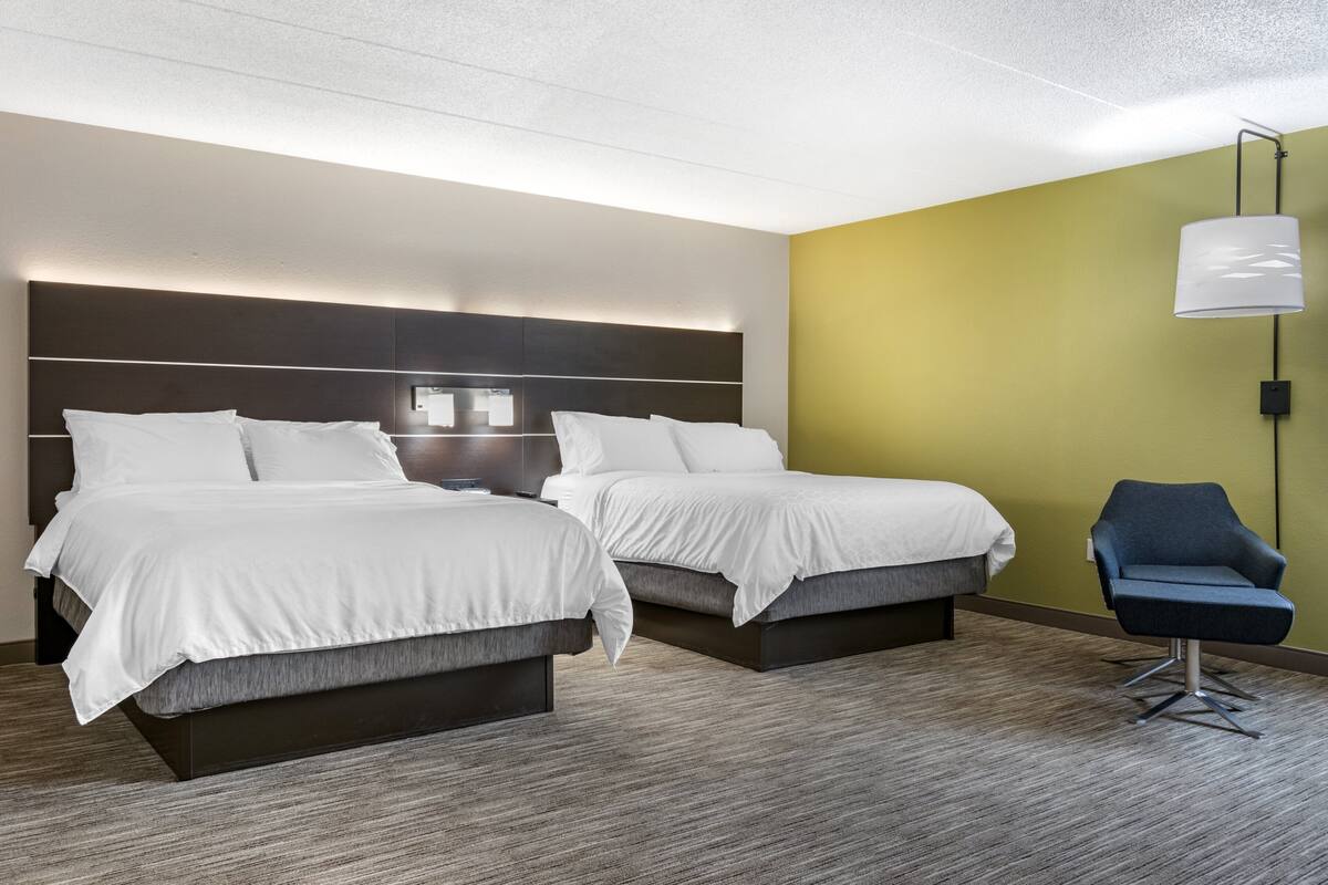 A hotel room with two beds, a nightstand, a desk, and a chair.