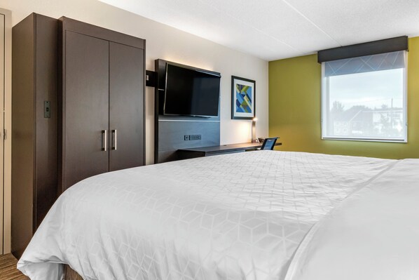 A hotel room with a large bed, a flat-screen TV, a desk with a chair, and a window with a view.