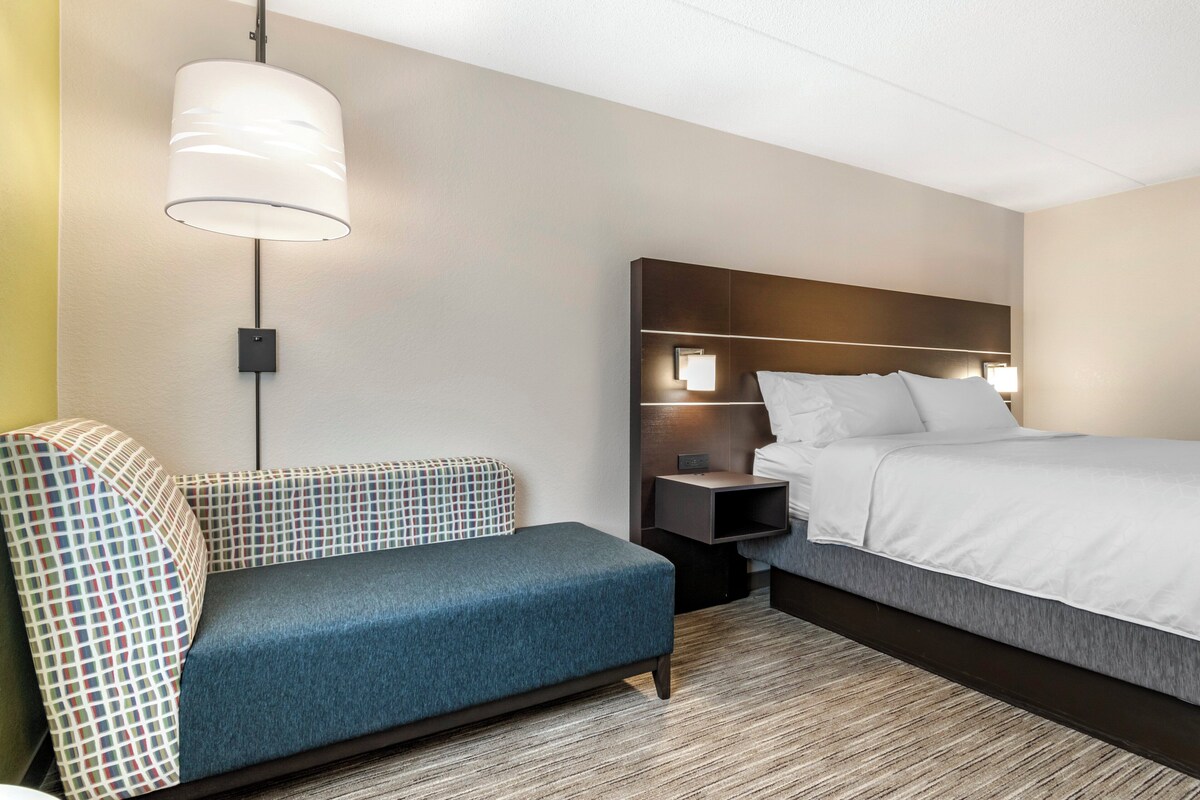 A hotel room with a bed, a bedside table, a lamp, and a sofa.