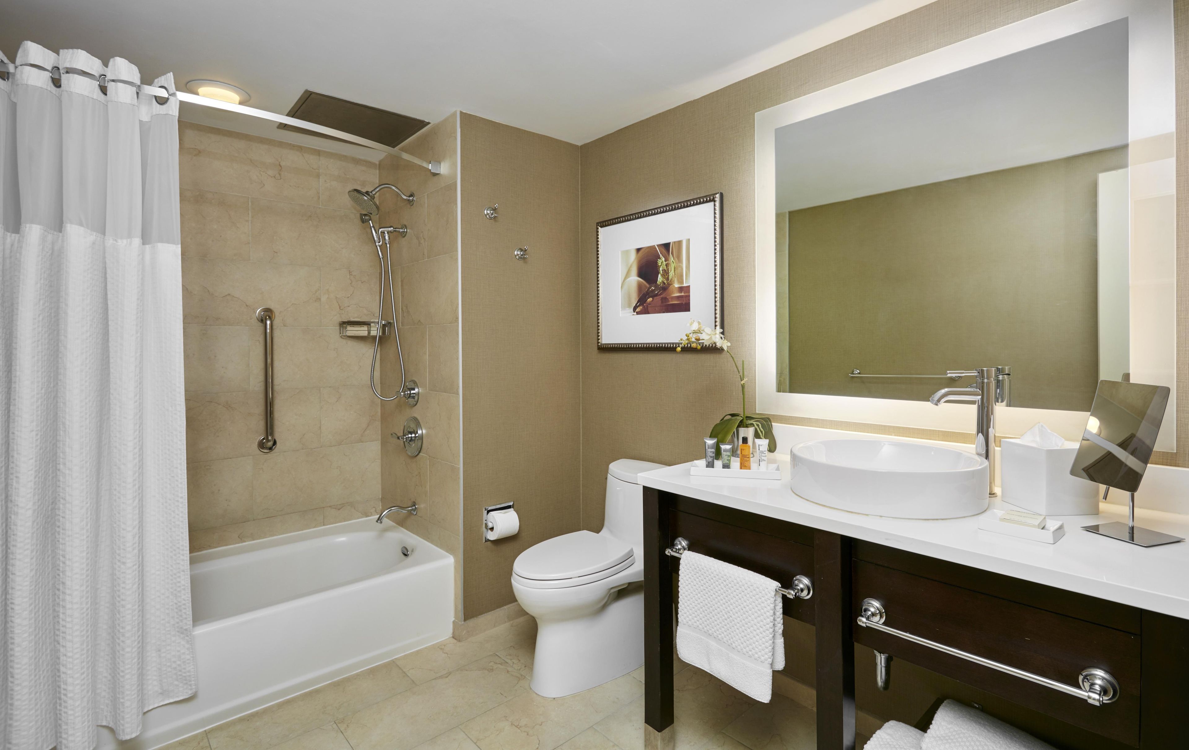 A modern bathroom with a bathtub, shower, toilet, vanity with sink, and a large mirror.