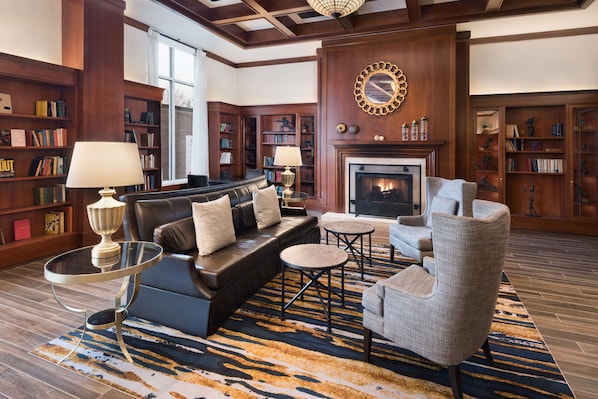 A spacious living room with a fireplace, leather sofa, armchairs, and a bookshelf filled with books.