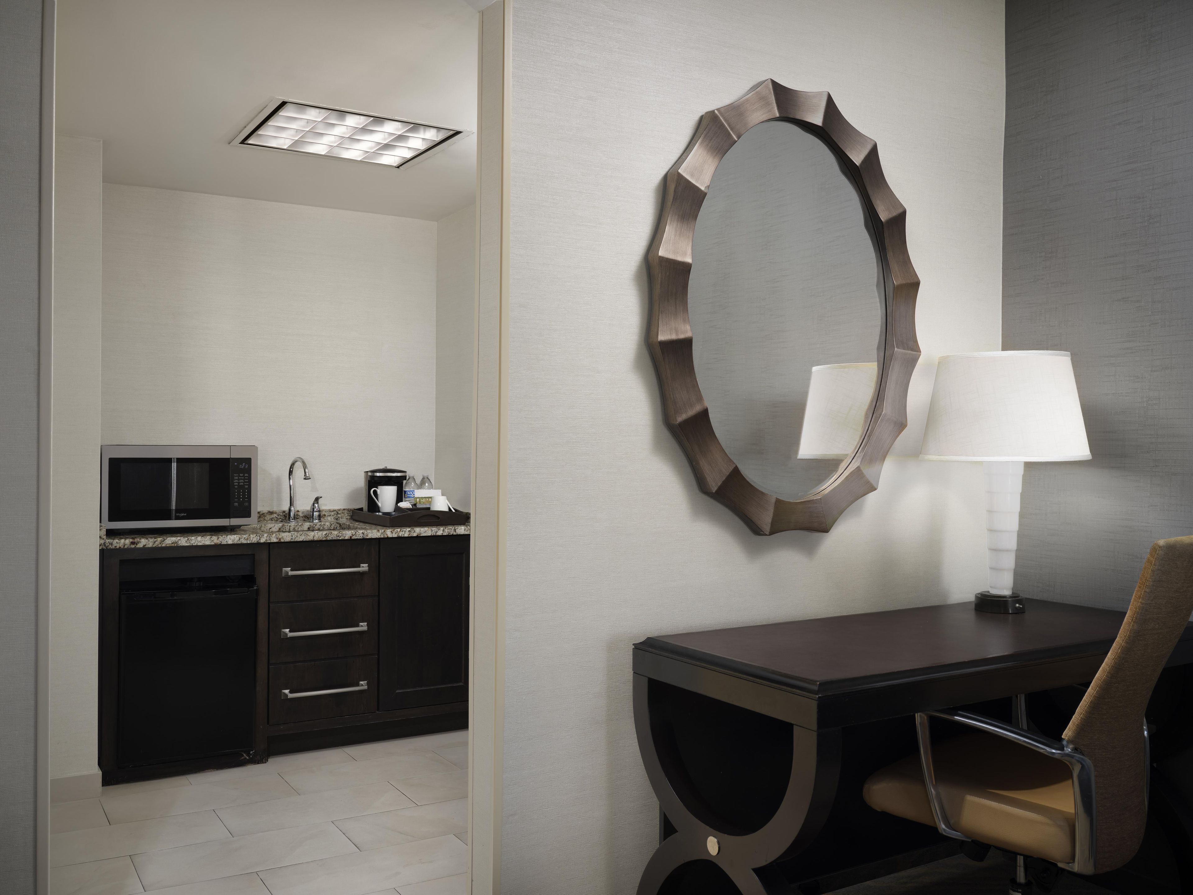 A modern bathroom with a vanity, a mirror, a microwave, and a table with a chair.