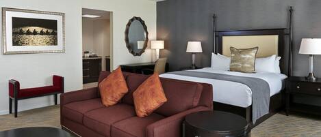 A hotel room with a bed, a sofa, a desk, a chair, and a dining area.