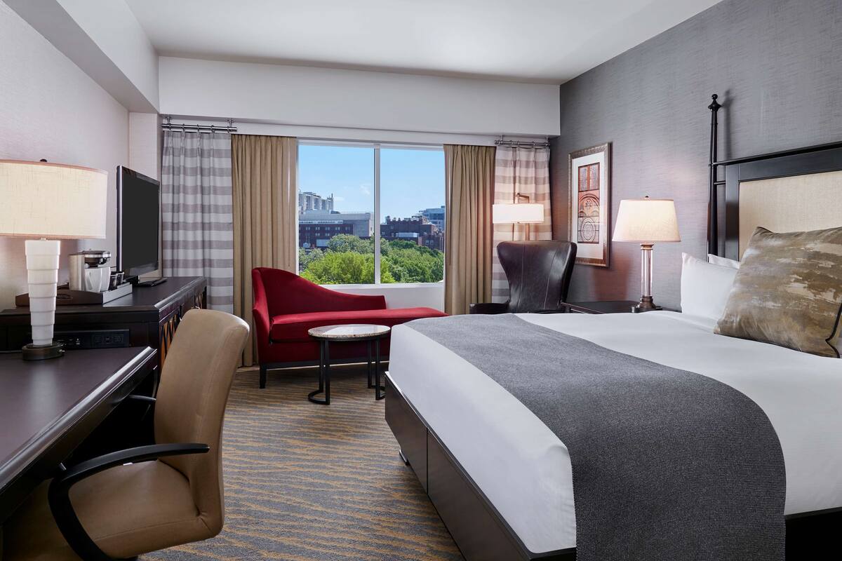 Une chambre d’hôtel avec un lit, un bureau, une chaise et une vue sur la ville.