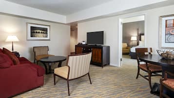 Une chambre d’hôtel avec un canapé rouge, une table ronde, un téléviseur et un coin repas avec des chaises.