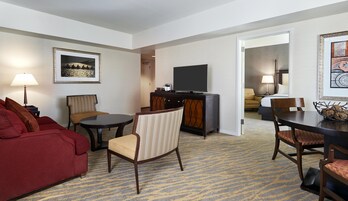A hotel room with a red sofa, a round table, a television, and a dining area with chairs.