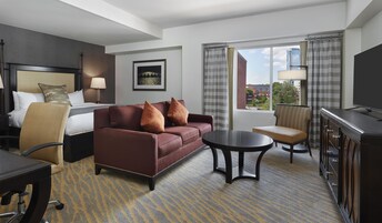 Habitación de hotel con cama, sofá, escritorio, silla, televisor y ventana con vistas a edificios.