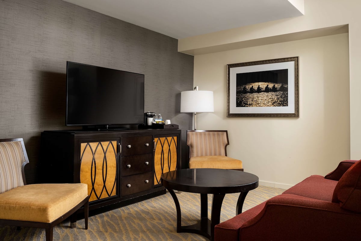 Une chambre d’hôtel équipée d’un téléviseur à écran plat, d’une commode avec des tiroirs, d’une table ronde, de deux fauteuils, d’un canapé, d’une lampe et d’un tableau encadré au mur.