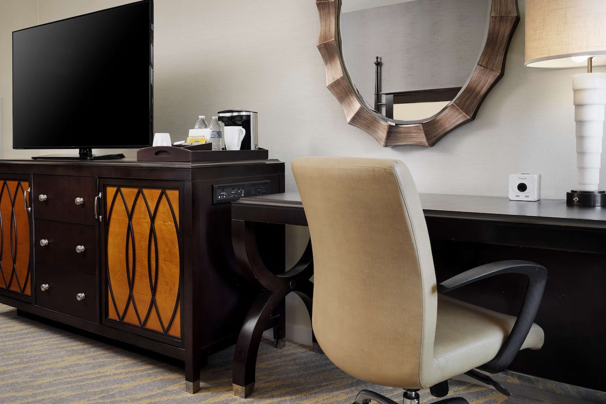 Une chambre d’hôtel équipée d’une télévision à écran plat, d’un bureau avec une lampe, d’une chaise et d’un miroir au mur.