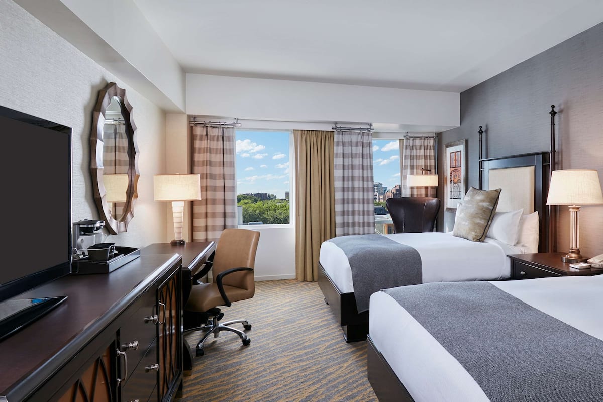 Une chambre d’hôtel avec deux lits, un bureau, une chaise, une télévision et une vue sur la ville.