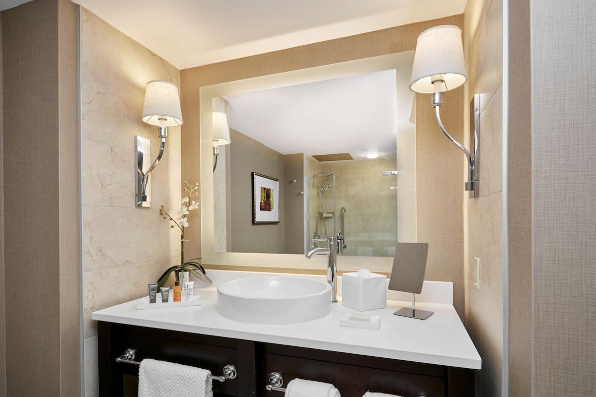 Une salle de bain moderne avec un grand miroir, un lavabo blanc et deux appliques murales.