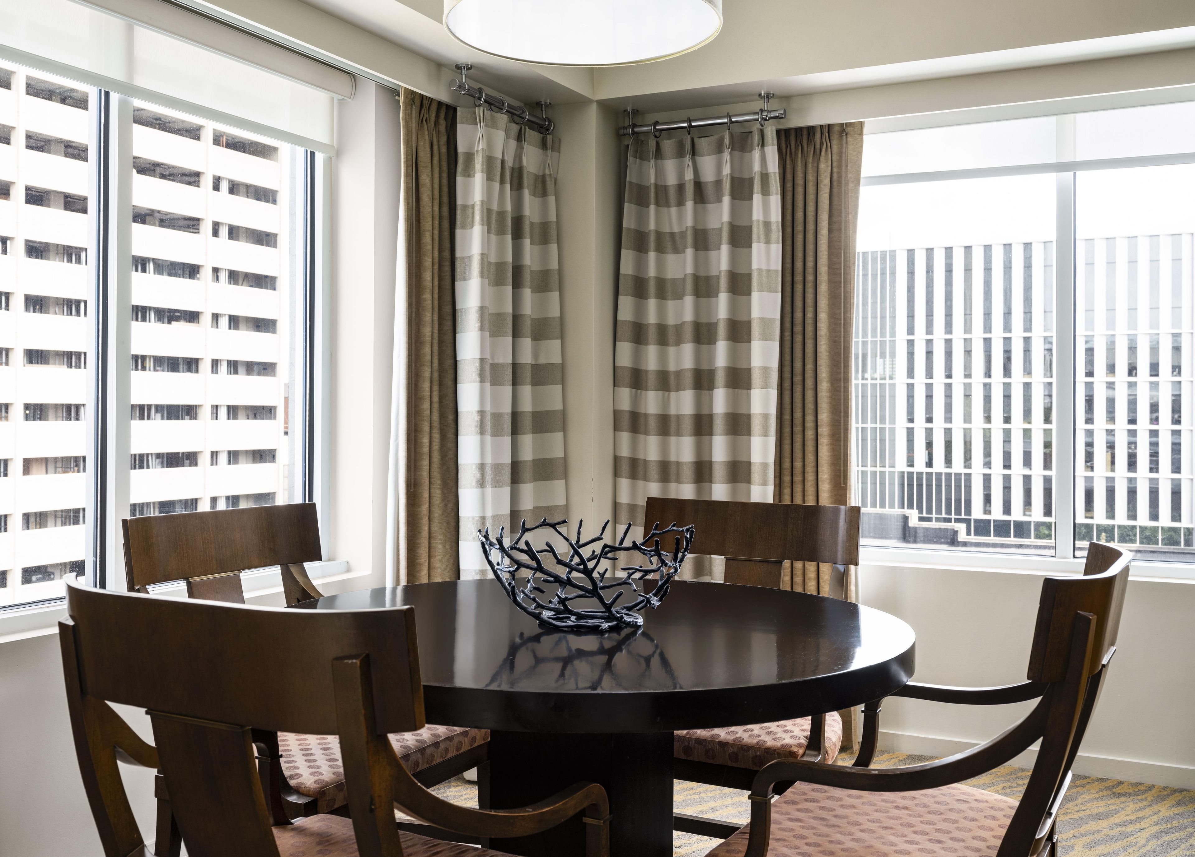 Un rincón comedor con una mesa redonda, cuatro sillas, un cuenco decorativo y cortinas.