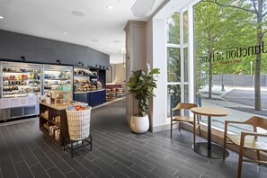 Un café doté d’une grande fenêtre, d’un espace salon avec des tables et des chaises, et d’un présentoir réfrigéré où sont exposées des boissons et des en-cas.