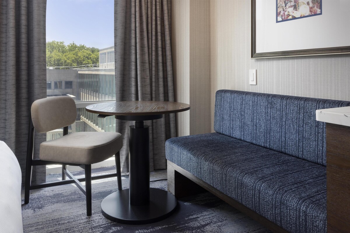 A hotel room with a sofa, a chair, a small round table, and a window with curtains.