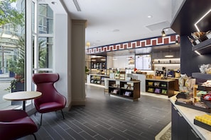 A modern cafe interior with seating, a counter with snacks, and a menu display. - The Inn at Penn, A Hilton Hotel (Philadelphia)
