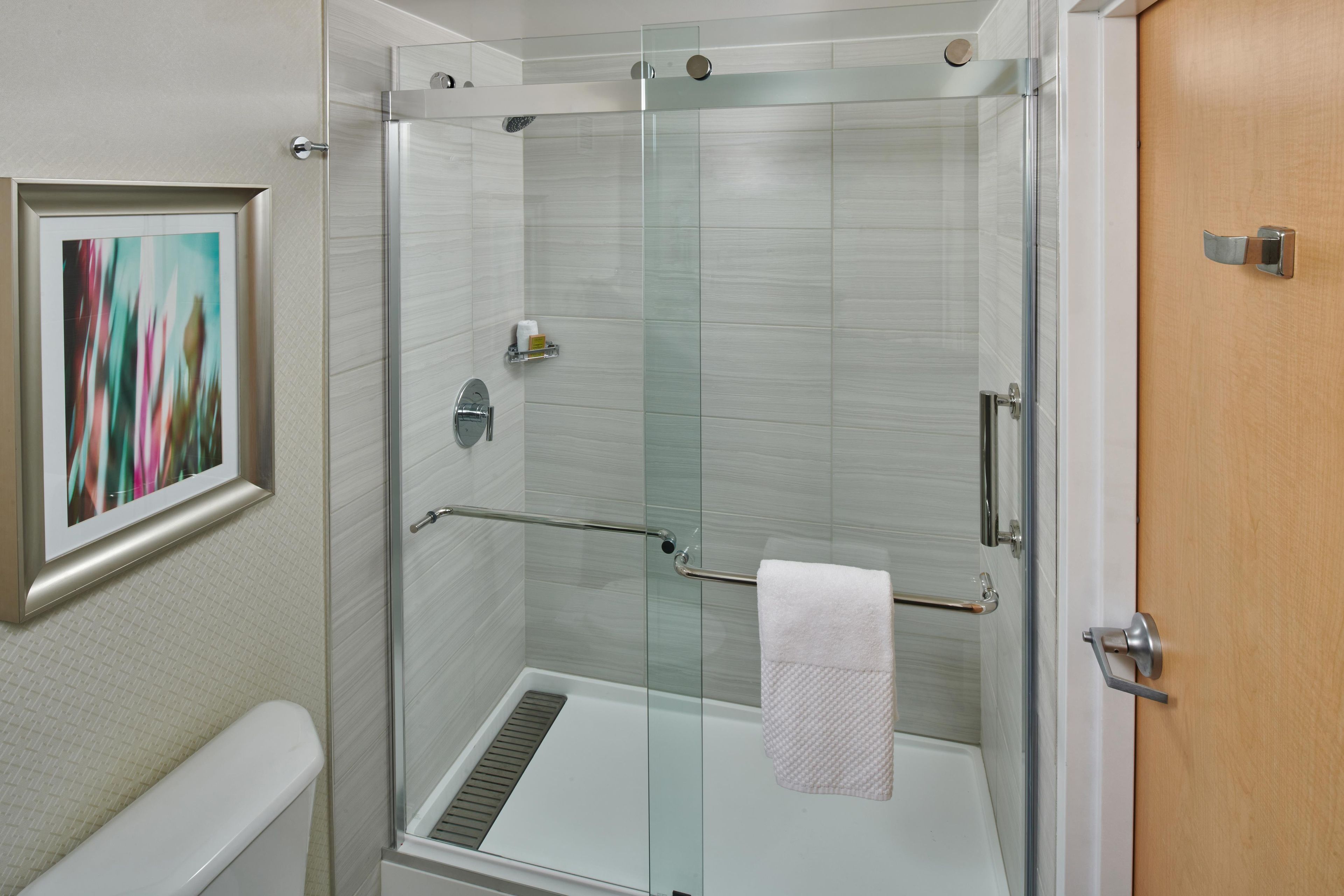 A modern bathroom with a glass-enclosed shower, a white toilet, and a framed abstract painting on the wall.