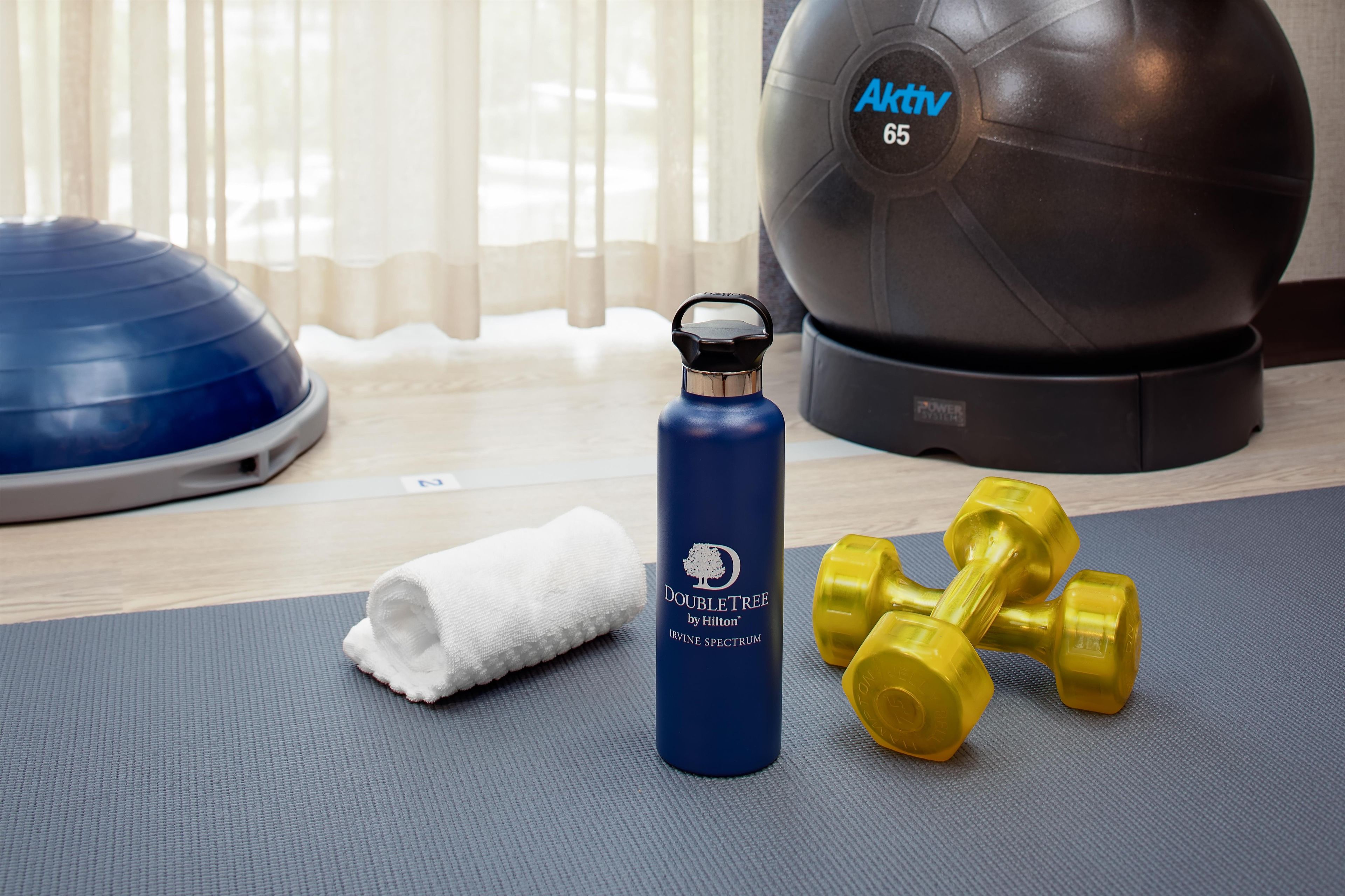 A fitness area with a blue exercise ball, yellow dumbbells, a water bottle, and a towel on a mat.