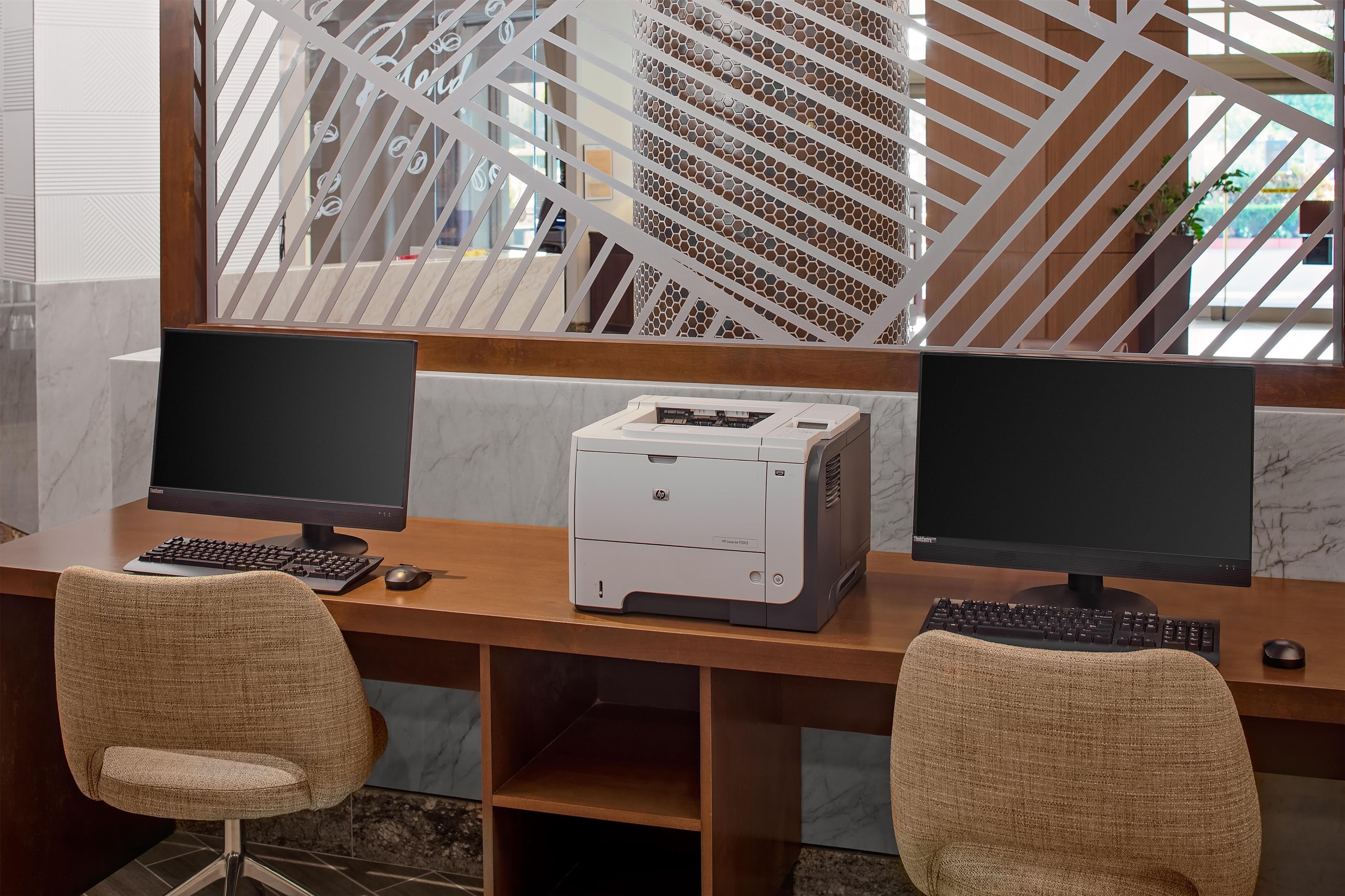 A workspace with two monitors, a printer, and two chairs.