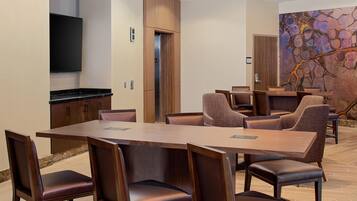 A conference room with a long table, multiple chairs, a television, and a door leading to another room.