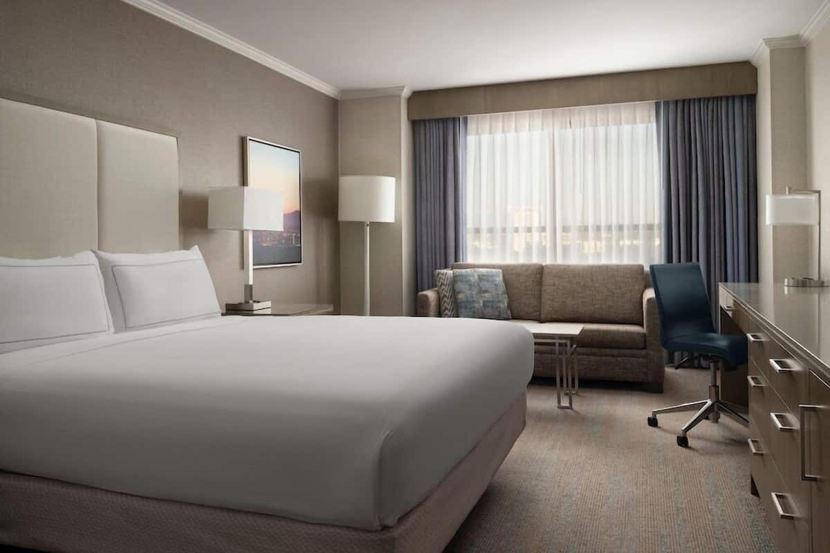 Una habitación de hotel con una cama grande, un escritorio, una silla, un sofá y una ventana con cortinas.